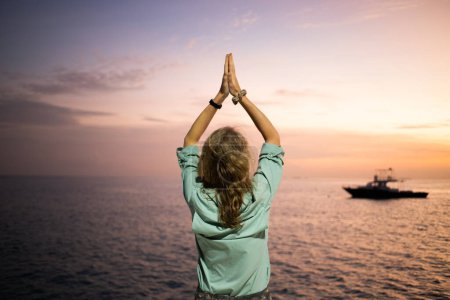 Téléchargez les photos : Femme faisant du yoga contre le coucher du soleil nuage sur l'océan - en image libre de droit