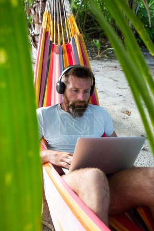 Téléchargez les photos : Homme travaillant sur ordinateur portable sur la plage exotique - en image libre de droit