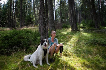 Foto de Mujer relajante en bosque de pinos con perro - Imagen libre de derechos