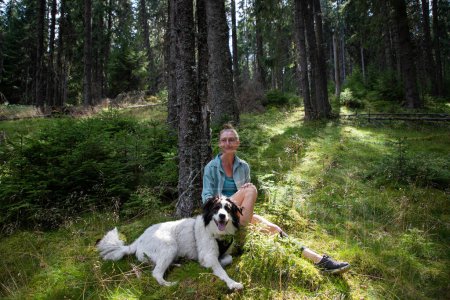Téléchargez les photos : Femme se relaxant dans la forêt de pins avec chien - en image libre de droit