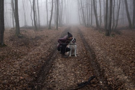 Téléchargez les photos : Femme avec chien dans la forêt brumeuse humide - en image libre de droit