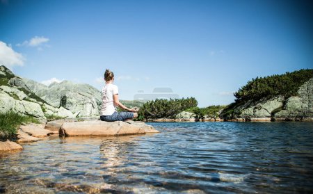 Foto de Mujer joven y saludable haciendo yoga en el paisaje de montaña junto al lago - Imagen libre de derechos