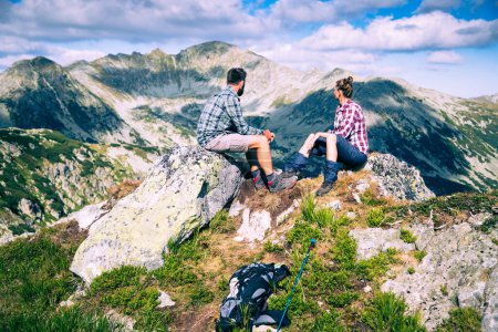 Téléchargez les photos : Couple assis sur le sommet de la montagne dans un paysage estival incroyable - en image libre de droit