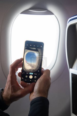 Téléchargez les photos : Homme prenant des photos par la fenêtre de l'avion - en image libre de droit