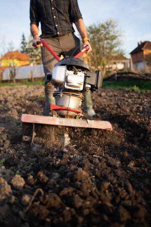 Téléchargez les photos : Agriculture biologique homme laboure le sol au coucher du soleil avec un tiller préparant le sol pour l'ensemencement - en image libre de droit