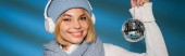 happy woman in winter hat and wireless headphones holding disco ball on blue, banner tote bag #619038952