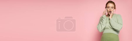 Photo for Shocked pregnant woman in sweater talking on cellphone on pink background, banner - Royalty Free Image