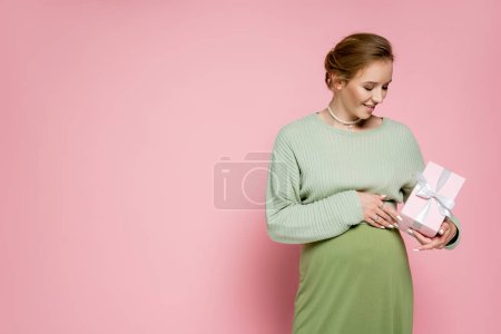 Téléchargez les photos : Heureuse femme enceinte en tenue verte tenant présente sur fond rose - en image libre de droit