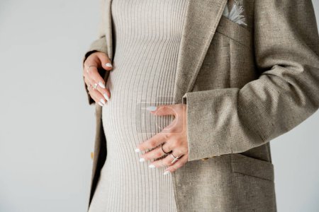Téléchargez les photos : Vue recadrée de la femme enceinte élégante en veste toucher le ventre isolé sur gris - en image libre de droit