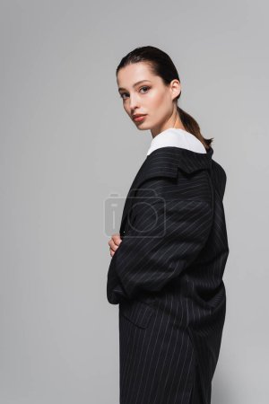 Téléchargez les photos : Brunette femme en veste noire regardant caméra isolée sur gris - en image libre de droit