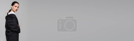 Téléchargez les photos : Jeune femme branchée en veste posant et regardant la caméra isolée sur gris, bannière - en image libre de droit