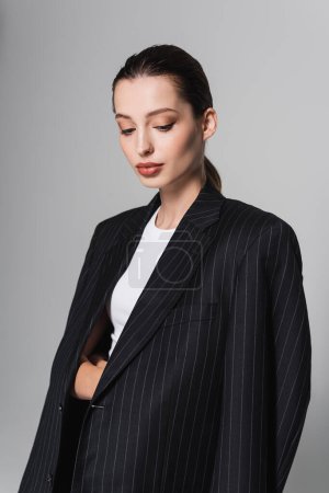 Téléchargez les photos : Femme élégante avec maquillage posant en veste noire isolée sur gris - en image libre de droit