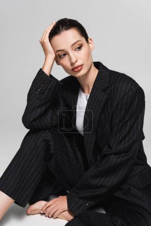 Téléchargez les photos : Jolie femme brune en costume assise sur fond gris - en image libre de droit