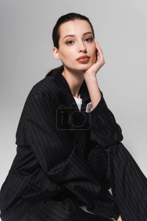 Téléchargez les photos : Portrait de jolie jeune femme en veste rayée regardant la caméra sur fond gris - en image libre de droit