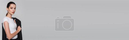 Téléchargez les photos : Jeune femme branchée en t-shirt tenant veste et regardant la caméra isolée sur gris, bannière - en image libre de droit