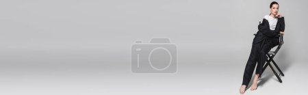 Téléchargez les photos : Femme pieds nus en costume posant sur chaise pliante sur fond gris, bannière - en image libre de droit