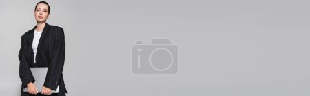 Téléchargez les photos : Jeune femme tendance en costume noir tenant ordinateur portable isolé sur gris, bannière - en image libre de droit