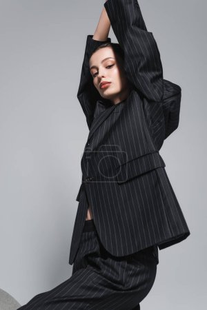 Téléchargez les photos : Jeune femme tendance avec maquillage en costume noir posant isolé sur gris - en image libre de droit