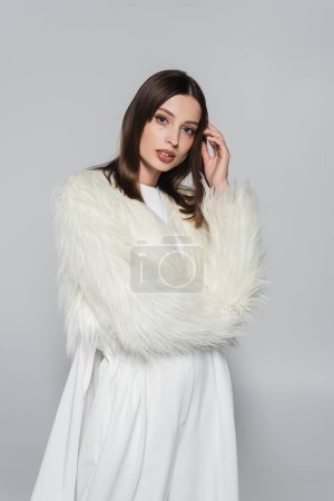 Téléchargez les photos : Portrait de la jeune femme élégante en fausse fourrure blanche regardant la caméra isolée sur gris - en image libre de droit