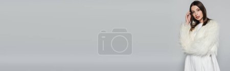 Téléchargez les photos : Portrait de jolie jeune femme en veste blanche élégante en fausse fourrure regardant la caméra isolée sur gris, bannière - en image libre de droit