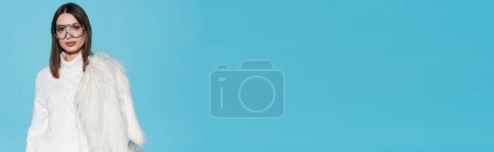 Téléchargez les photos : Élégant jeune femme dans des lunettes de vue à la mode et col roulé tenant veste en fausse fourrure blanche sur bleu, bannière - en image libre de droit