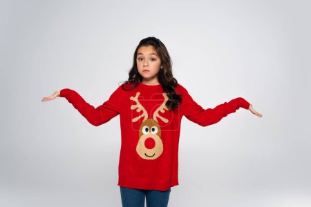 Preteen girl in festive sweater showing shrug gesture isolated on grey 
