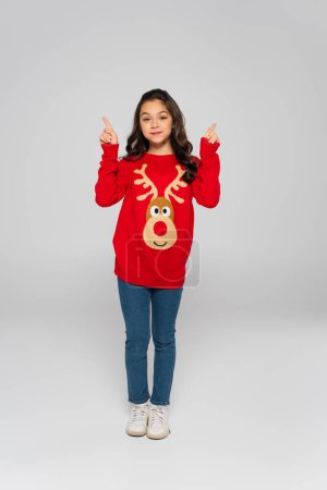 Full length of kid in new year sweater pointing with fingers on grey background 