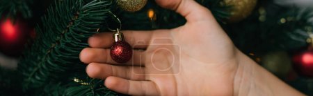 Cropped view of kid touching festive ball on Christmas tree, banner 