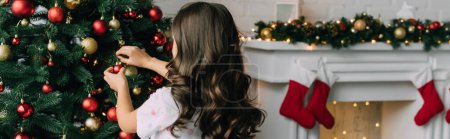 Preteen kid decorating Christmas tree near blurred fireplace at home, banner 