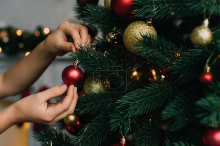 Ausgeschnittene Ansicht eines Kindes, das Tanne mit Weihnachtskugel zu Hause schmückt 