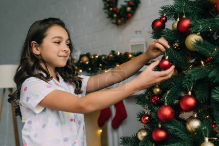 Lächelndes Mädchen schmückt Weihnachtsbaum im Wohnzimmer 