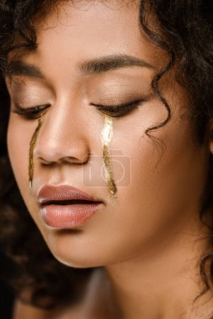 close up of african american woman with golden tears on cheeks looking down
