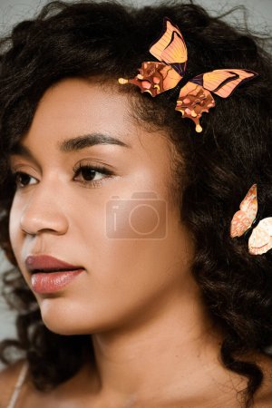 primer plano de mujer afroamericana bonita con mariposas en el pelo posando aislado en gris