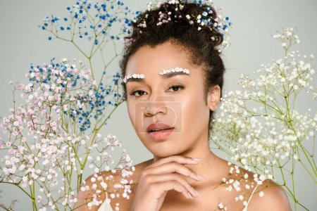 Photo for African american woman with flowers in hair looking at camera near gypsophila isolated on grey - Royalty Free Image