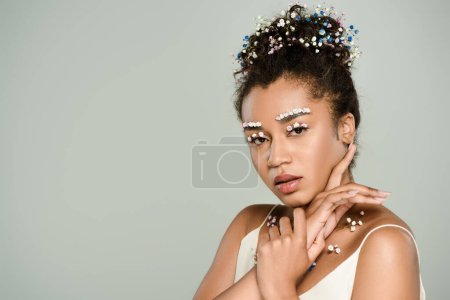 young african american woman with flowers on eyebrows and eyes posing isolated on grey