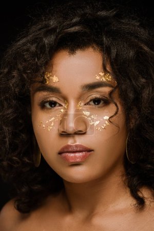 Téléchargez les photos : Brunette afro-américaine avec de la peinture corporelle dorée sur les joues isolées sur noir - en image libre de droit
