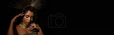 young african american woman with golden necklace and crown posing isolated on black, banner