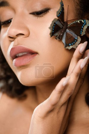 primer plano de sensual y joven mujer afroamericana con mariposa en la mejilla 