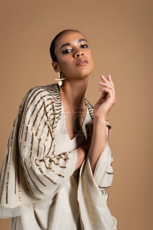 Photo for Young african american woman in golden earrings looking at camera isolated on beige - Royalty Free Image