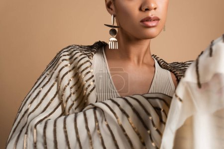 Téléchargez les photos : Vue recadrée de riche femme afro-américaine en bijoux dorés posant avec châle isolé sur beige - en image libre de droit