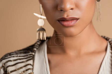 vue recadrée de femme afro-américaine en boucles d'oreilles dorées posant isolées sur beige 
