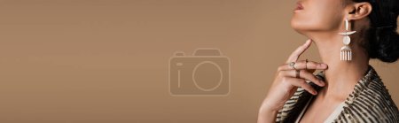 Téléchargez les photos : Vue recadrée de jeune femme afro-américaine en luxueux bijoux dorés posant isolée sur beige, bannière - en image libre de droit