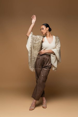Afrikanische Amerikanerin in Goldschmuck und Schal posiert in voller Länge auf beige 