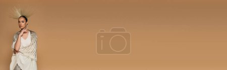 Téléchargez les photos : Brunette afro-américaine en châle brillant et couronne dorée regardant la caméra isolée sur beige, bannière - en image libre de droit
