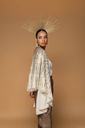brunette african american woman in earrings and golden crown posing isolated on beige 