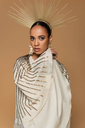 confident african american woman in shiny shawl and golden crown looking at camera isolated on beige  Stickers 620708444