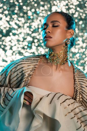 brunette african american woman with closed eyes posing with gold foil on neck on shiny blue background 