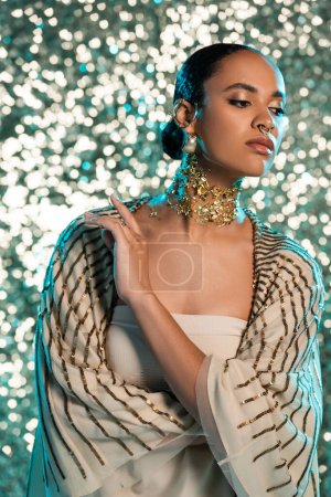 pierced african american woman with gold foil on neck and earrings posing on shiny blue background 