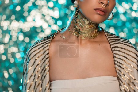 cropped view of african american woman with piercing and gold on neck posing on sparkling blue background 