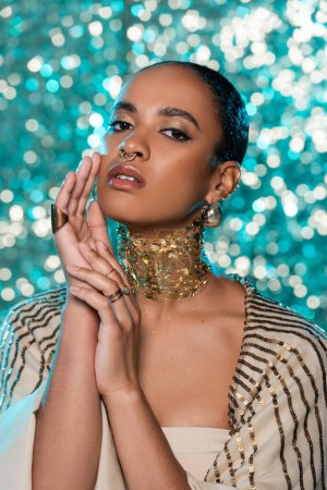 Téléchargez les photos : Brunette afro-américaine avec châle brillant et or sur le cou posant sur fond bleu étincelant - en image libre de droit